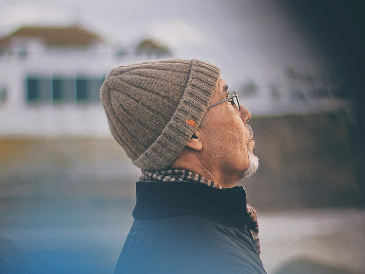 Nahaufnahme von einem &auml;lteren Mann mit einer M&uuml;tze drau&szlig;end stehend und in die ferne schauend